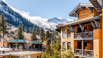 A mountain lodge with a wooden facade, a covered outdoor seating area, and a view of snow-capped mountains.