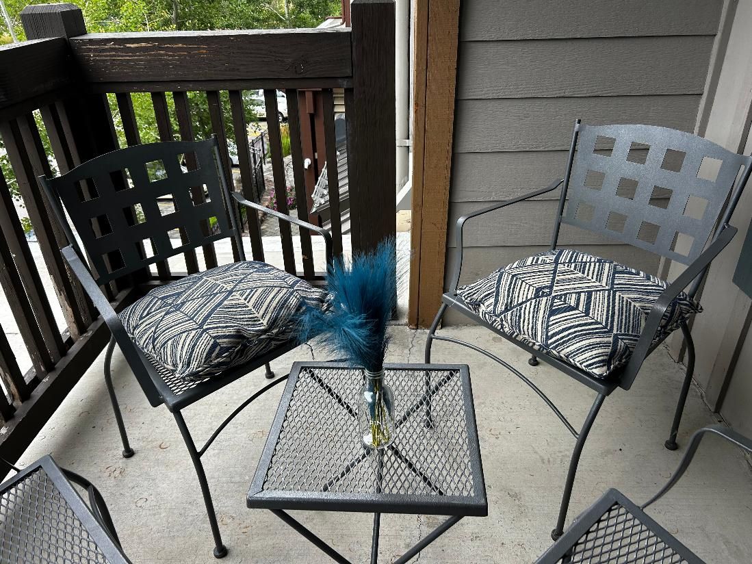 A patio area with two metal chairs and a small table, featuring a decorative vase with a feather.