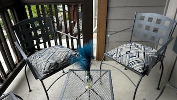 A patio area with two metal chairs and a small table, featuring a decorative vase with a feather.