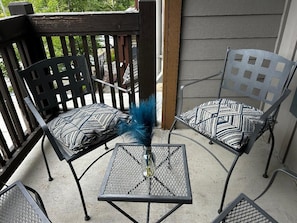A patio area with two metal chairs and a small table, featuring a decorative vase with a feather.