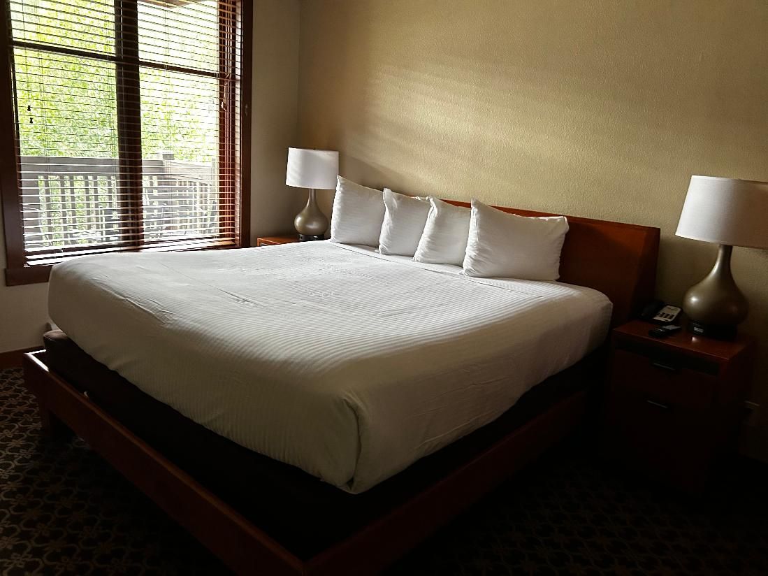 Una habitación de hotel con una cama grande, dos mesitas de noche con lámparas y una ventana con persianas.