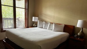 Quarto de hotel com uma cama grande, duas mesas de cabeceira com abajures e uma janela com persianas.