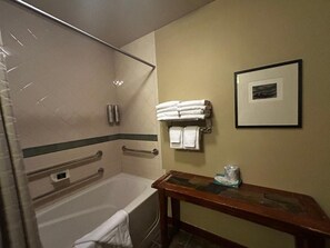 A bathroom with a bathtub, a shower, a towel rack with folded towels, a framed picture on the wall, and a wooden bench with a towel and a bottle. - Well appointed Ski-in Ski out cozy 1-bedroom condo walking distance from slopes. (Olympic Valley)