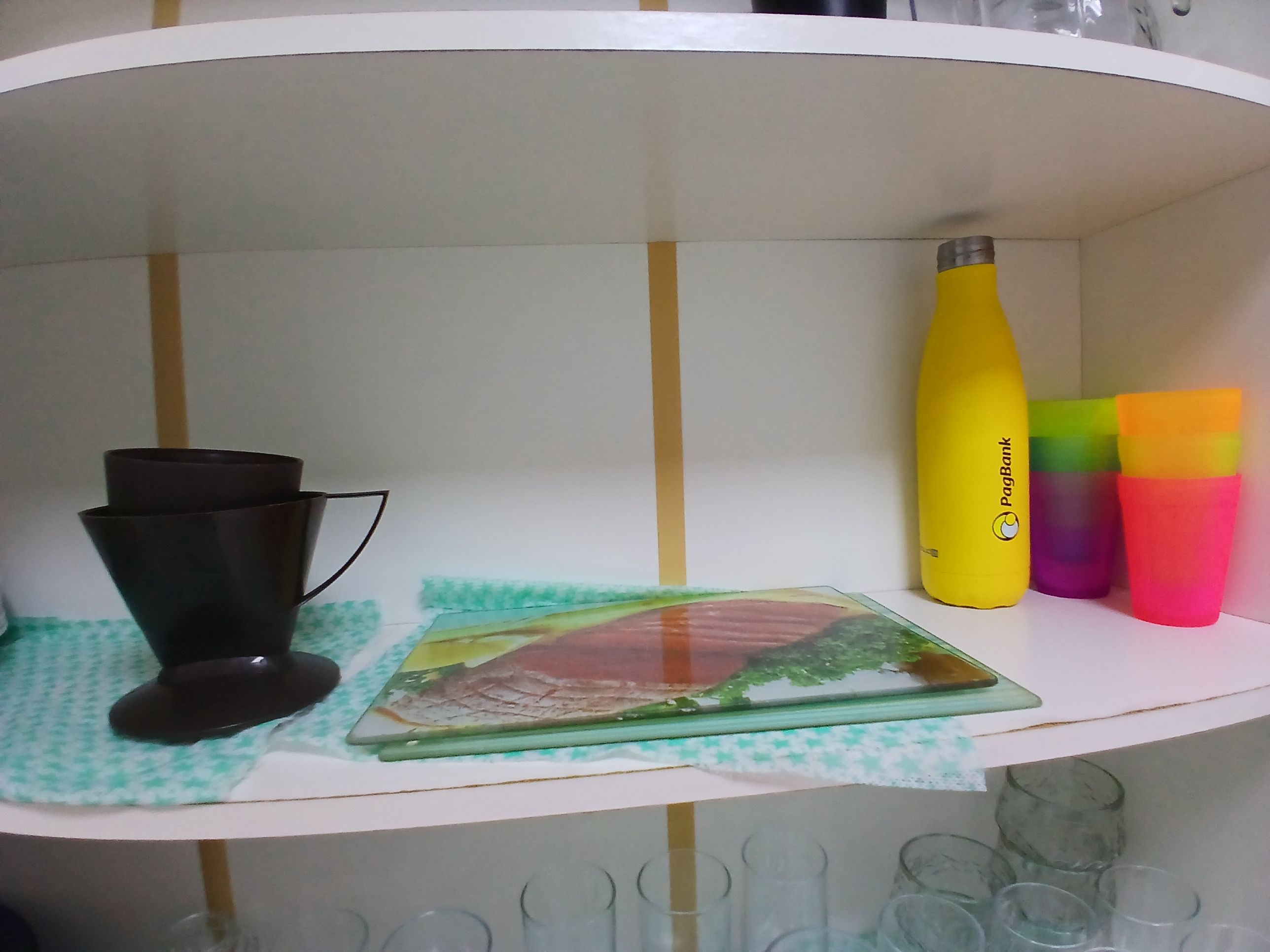 Een plank met een zwart object, een gele fles en een beker met alle kleuren van de regenboog.