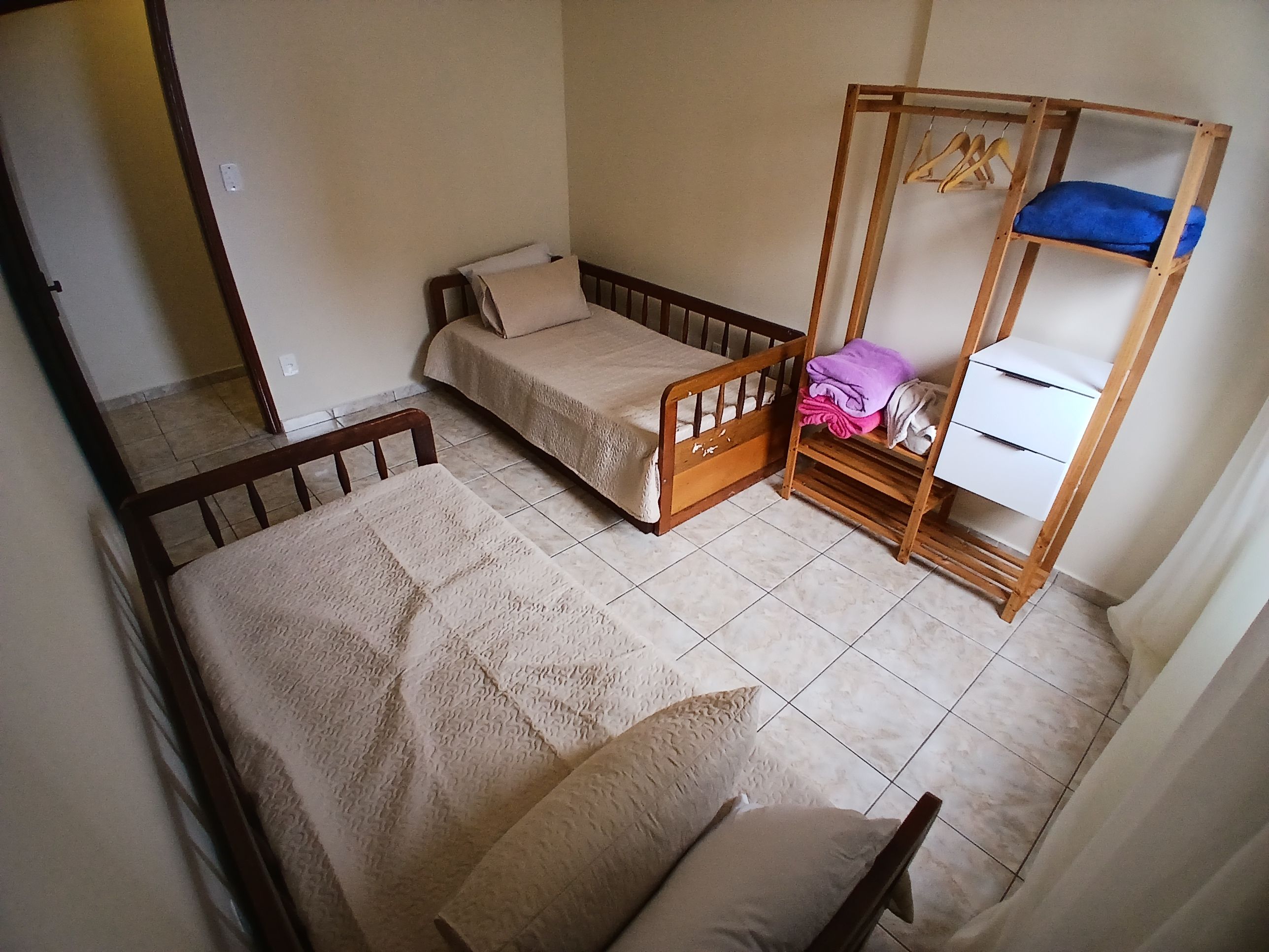 Alojamento pequeno e individual, com uma cama, guarda-roupa de madeira e uma mesa pequena.