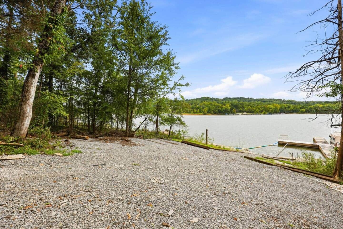 Une zone recouverte de gravier avec une jetée qui s’avance sur un lac paisible, le tout entouré d’arbres.