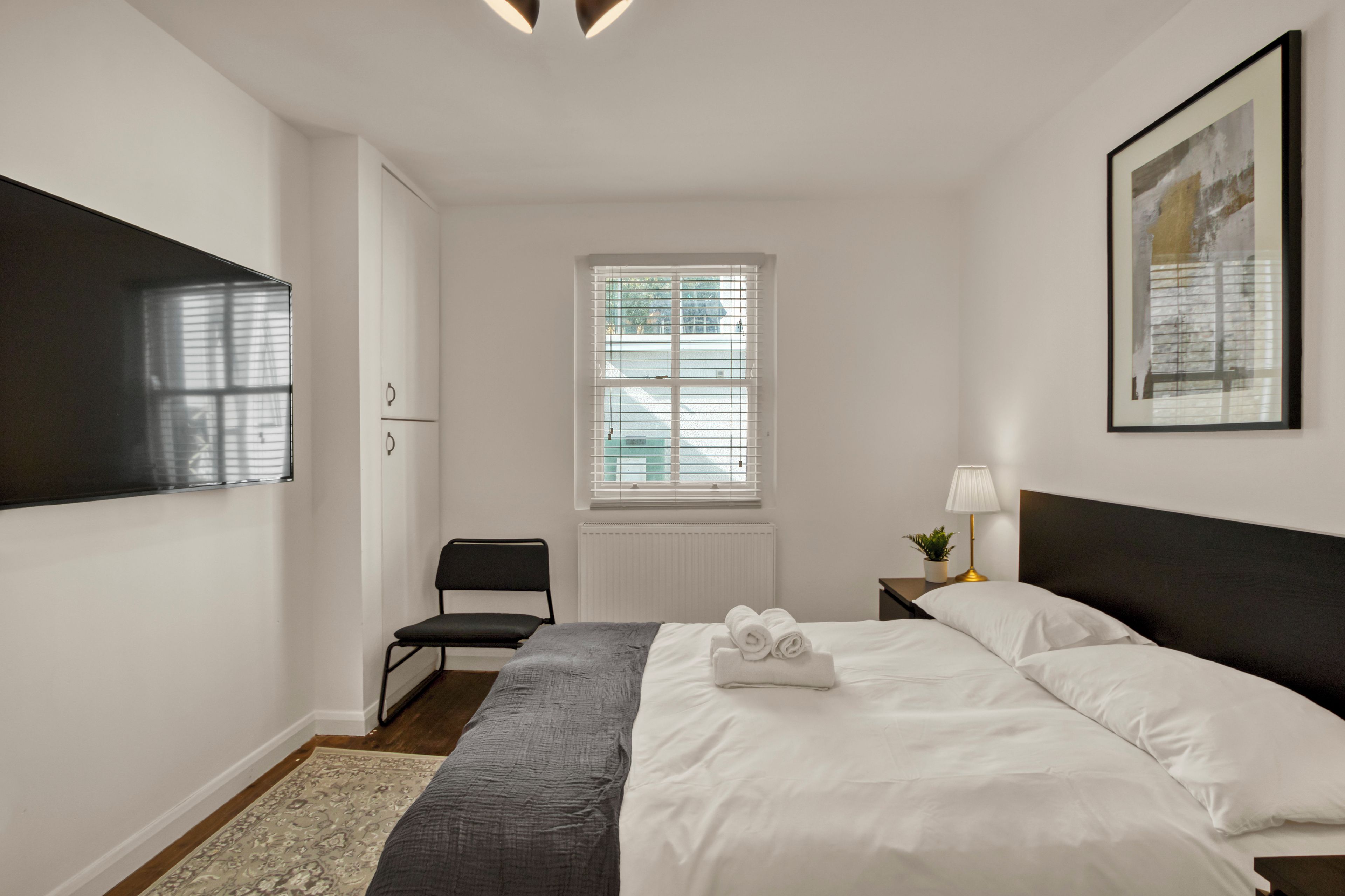 Een hotelkamer met een bed, een stoel, een raam, een radiator en een tv aan de muur.