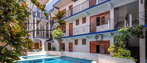 A multi-story hotel with a swimming pool, balconies, and a garden area.