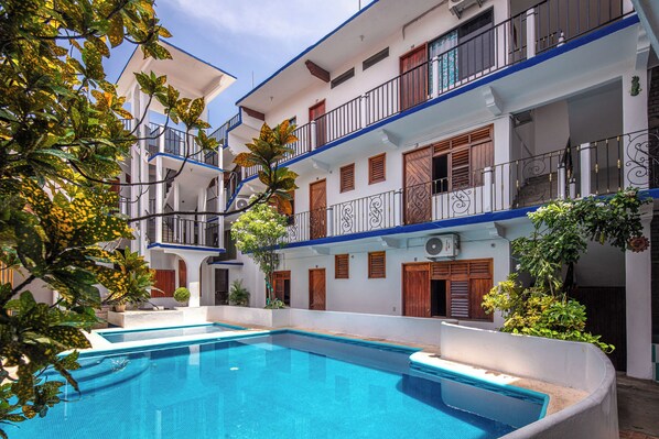 A multi-story hotel with a swimming pool, balconies, and a garden area.