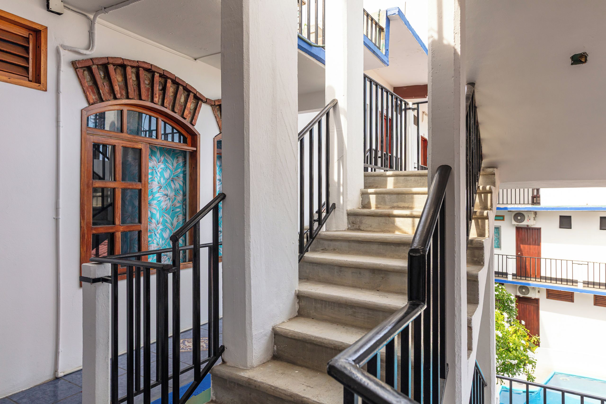 Una escalera con barandilla, un ventanal con diseño decorativo y vistas de un edificio con balcones.