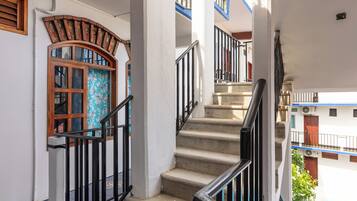 Una escalera con barandilla, un ventanal con diseño decorativo y vistas de un edificio con balcones.