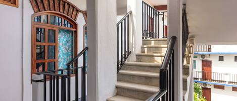 Una escalera con barandilla, un ventanal con diseño decorativo y vistas de un edificio con balcones.