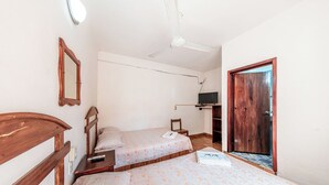 Un dormitorio con dos camas, ventilador de techo, televisión y puerta de madera.