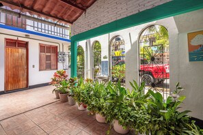 A covered outdoor area with a tiled floor, potted plants, and a red vehicle parked outside.