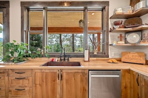 A kitchen with wooden cabinets, a stainless steel dishwasher, a window with a view of trees, and a shelf with kitchen items. - Fall Escape Special: 15% Discount Ends Nov 30! Must book by Oct 18 (Pagosa Springs)