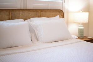 A neatly made bed with white bedding and pillows, a woven headboard, and a bedside table with a lamp and a phone. - NEW LISTING! The Swan on Park: Historic Charm near Lake Hollingsworth & FSC (Lakeland)
