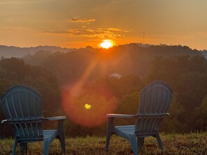 Zwei Adirondack-Stühle, die auf eine Landschaft mit Hügeln bei Sonnenuntergang ausgerichtet sind.