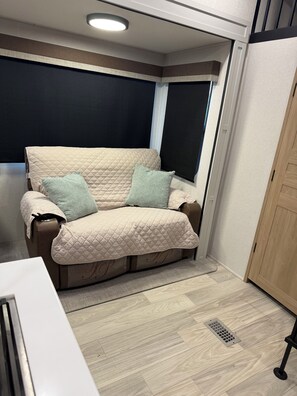 Ein Zimmer mit einem beigen, gesteppten Sofa, zwei Kissen, einem weißen Tisch und einem Holzschrank.