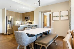 A modern kitchen with a dining area, wooden cabinets, stainless steel appliances, and a bench. - Charlie Rentz: Remodeled, 2 Balconies, Ski-In/Out w/ Valet, Resort Amenities, Pool + Hot Tubs (Avon)
