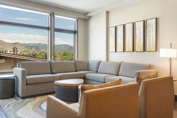 A modern living room with a sectional sofa, a round coffee table, and a view of mountains through large windows. - Charlie Rentz: Remodeled, 2 Balconies, Ski-In/Out w/ Valet, Resort Amenities, Pool + Hot Tubs (Avon)