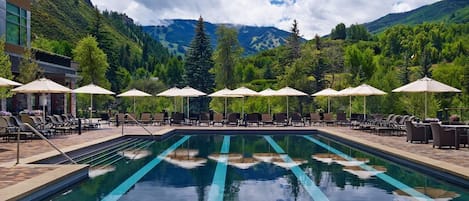 A swimming pool with lounge chairs and umbrellas, surrounded by mountains and trees.