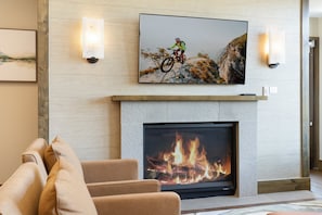 A living room with a fireplace, a mounted television, and a sofa with cushions. - Charlie Rentz: Remodeled, 2 Balconies, Ski-In/Out w/ Valet, Resort Amenities, Pool + Hot Tubs (Avon)