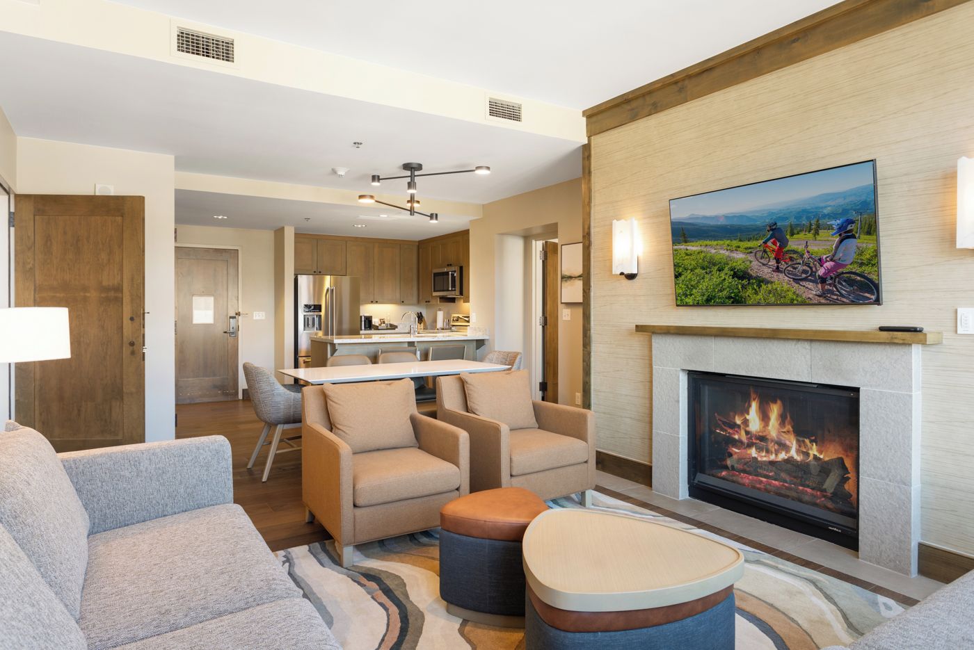 A modern hotel room with a fireplace, a dining area, and a view of the mountains.