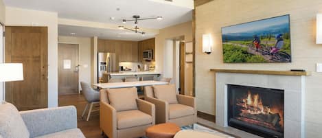 A modern hotel room with a fireplace, a dining area, and a view of the mountains.