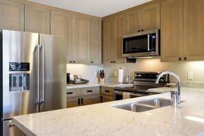 A modern kitchen with stainless steel appliances, wooden cabinets, granite countertops, and a double sink. - Charlie Rentz: Remodeled, 2 Balconies, Ski-In/Out w/ Valet, Resort Amenities, Pool + Hot Tubs (Avon)