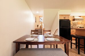 Un coin repas avec une table en bois dressée pour quatre personnes, une cuisine avec des meubles en bois et un réfrigérateur noir.