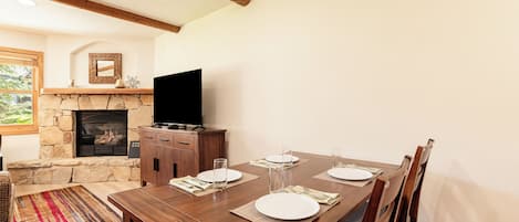 Uma sala de jantar com lareira de pedra, mesa de madeira e cadeiras.
