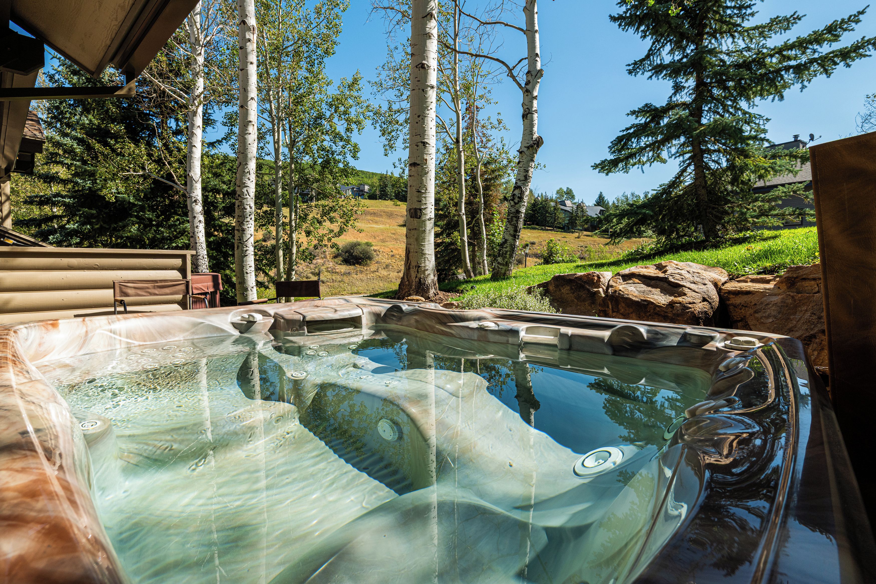 Ein Whirlpool mit freiem Blick auf die umliegende Landschaft, darunter Bäume und ein entferntes Gebäude.