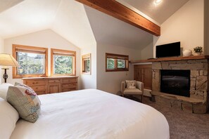 Une chambre à coucher avec un grand lit, une tête de lit en bois, une cheminée en pierre et un téléviseur placé au-dessus.