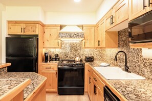 A kitchen with wooden cabinets, a black refrigerator, a stove, a sink, and granite countertops. - Walk to Slopes, Dining & Old Town (Park City)