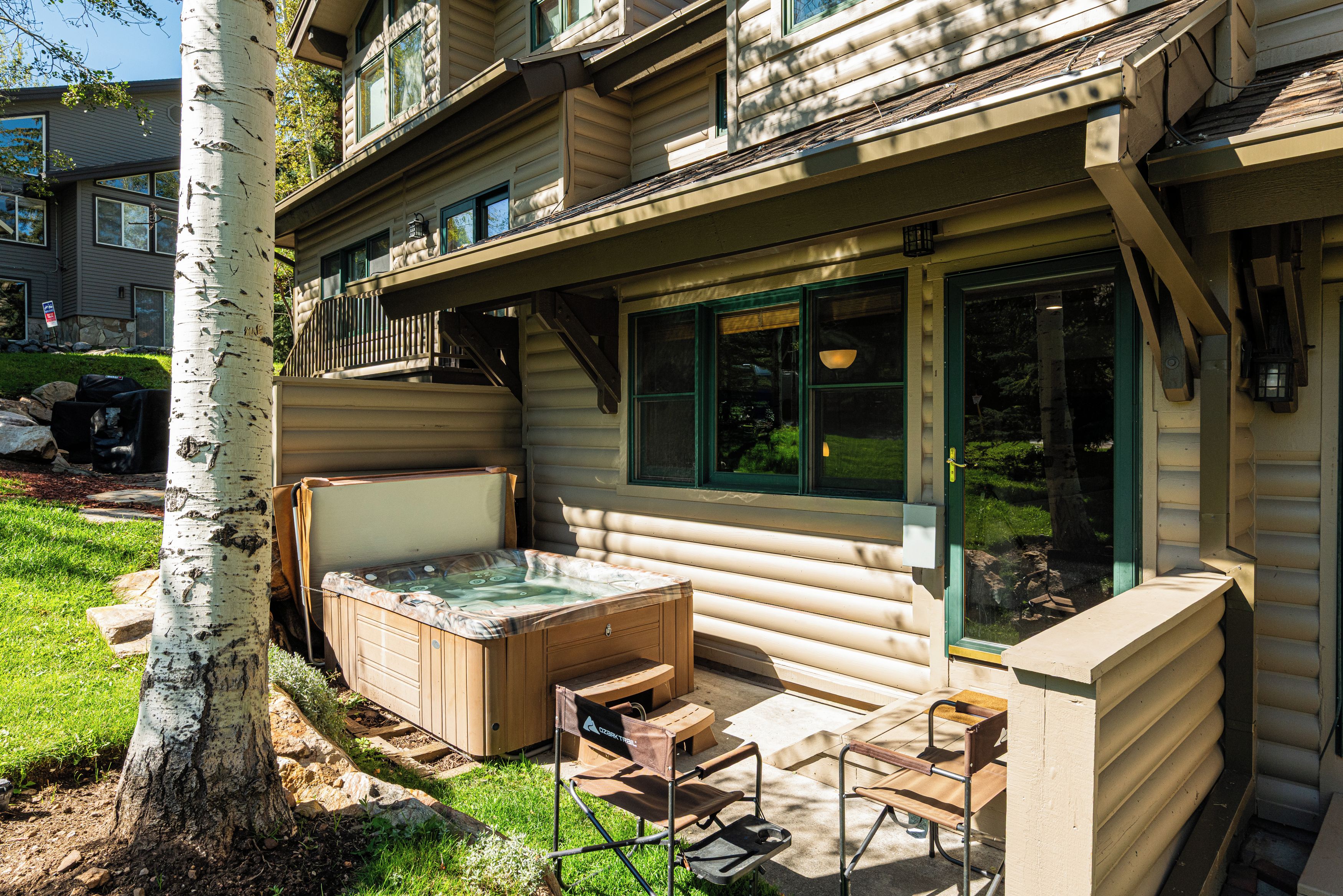 A log cabin with a hot tub, outdoor seating, and a large window.