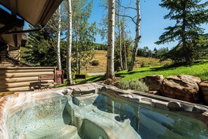 A hot tub in a landscaped outdoor area with a wooden deck, a bench, and a view of a hillside with trees and a house. - Walk to Slopes, Dining & Old Town (Park City)