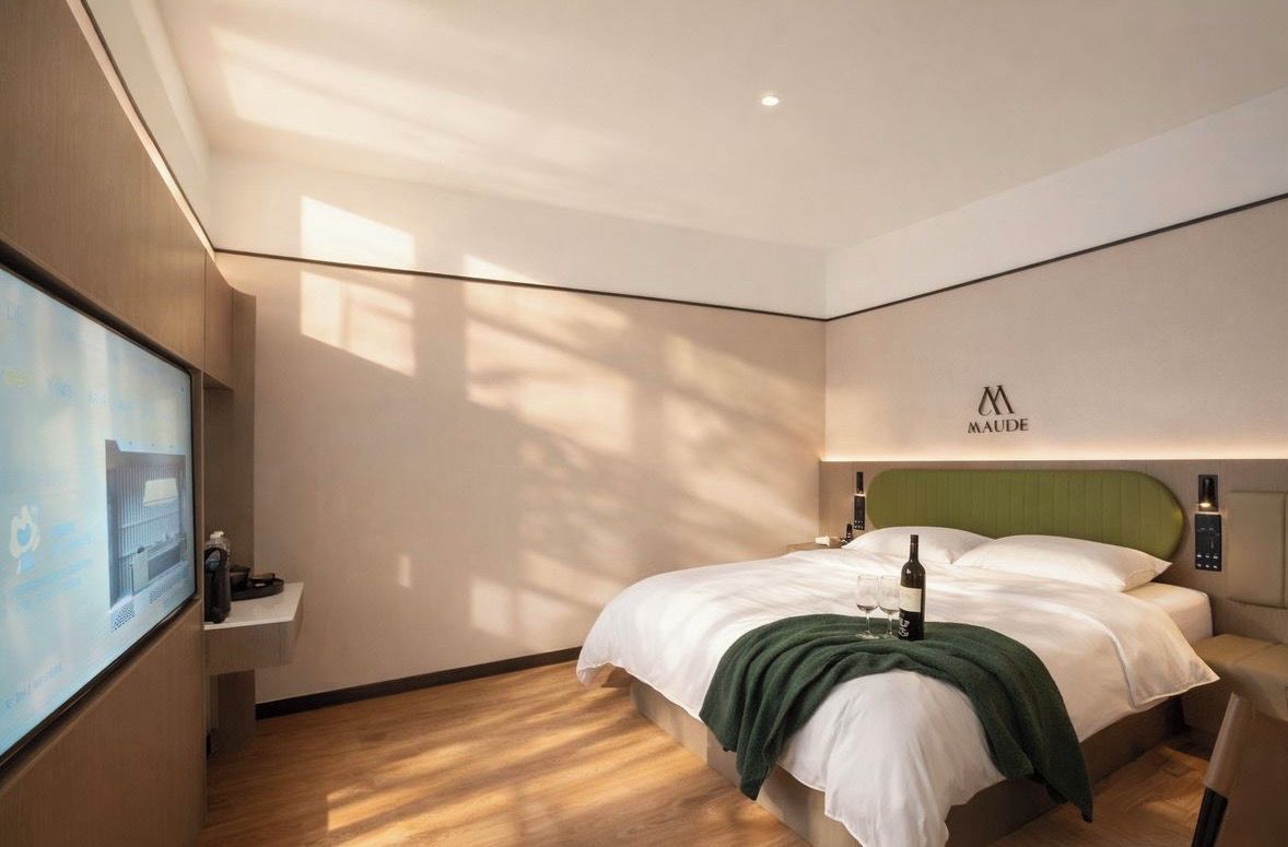 A hotel room with a bed, a television on the wall, and a logo on the headboard.