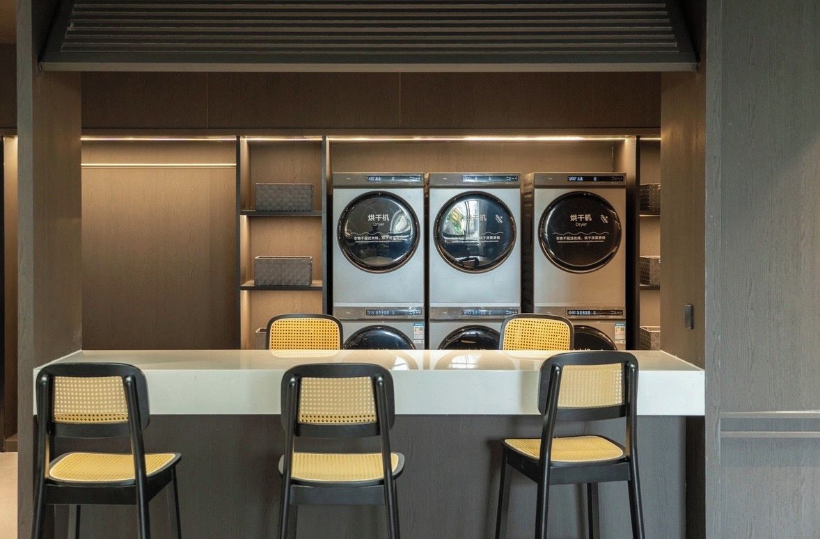 Een wasruimte met drie wasmachines en een tafel met stoelen.