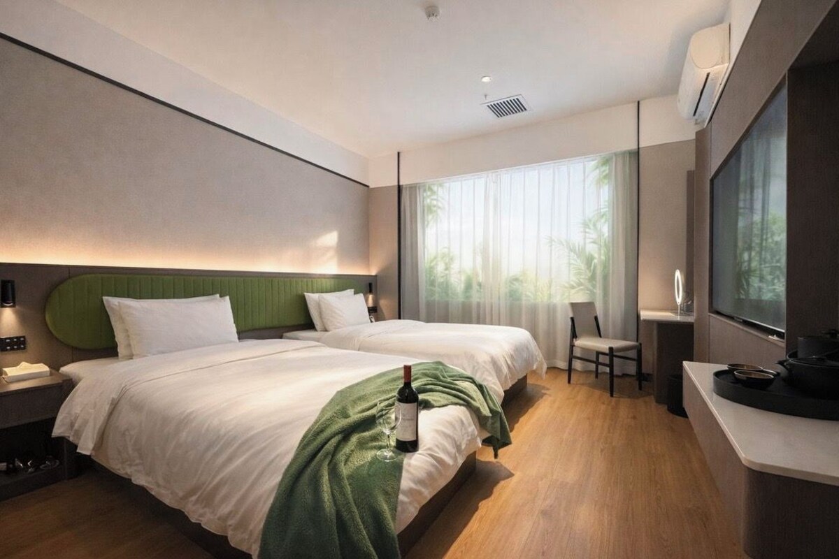 Habitació d'hotel amb dos llits, una taula petita, una cadira i una finestra gran amb cortines.