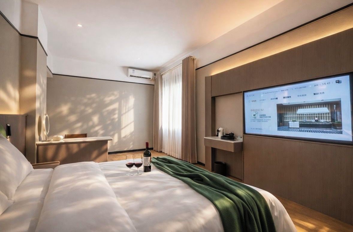 Een hotelkamer met een bed, een bureau, een televisiescherm en een raam met gordijnen.