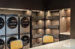 Un cuarto de lavandería con varias secadoras y lavadoras, repisas con cestas y un lavamanos.