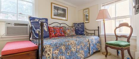 A bedroom with a bed, a chair, a bedside table, and a window.
