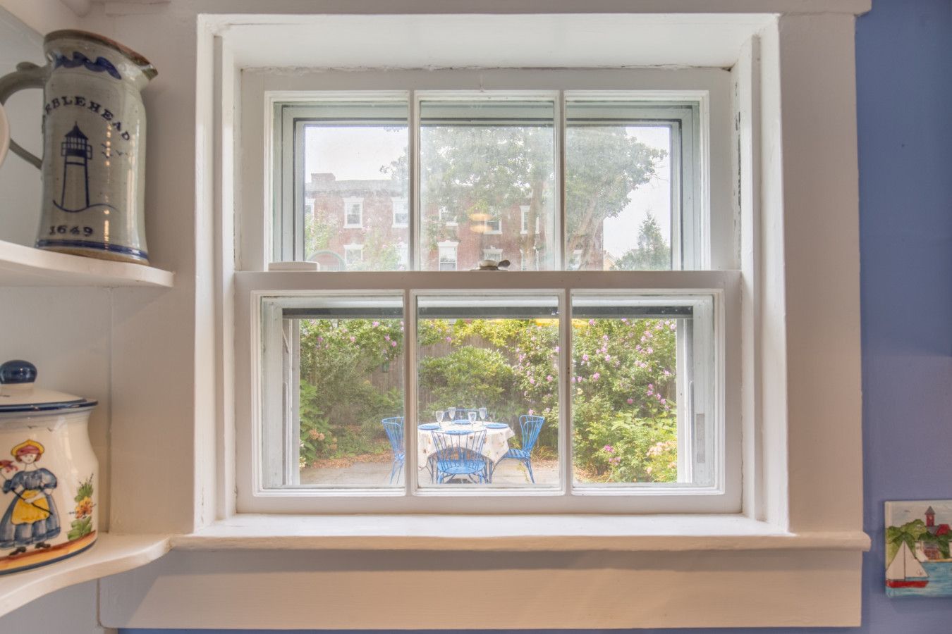 A window with a view of a garden and a table with chairs outside.