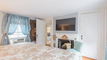 Een slaapkamer met een groot bed, een open haard, een televisie erboven en een deur naar een andere kamer.