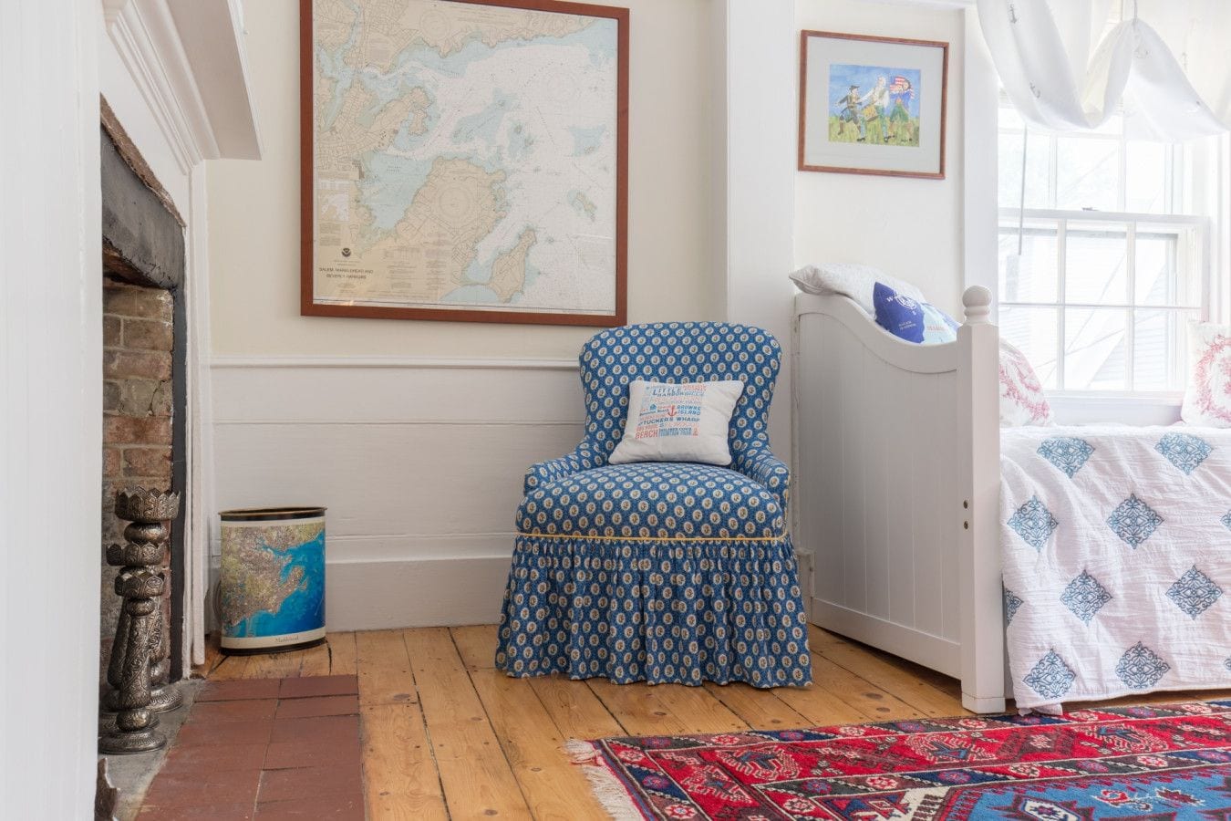 Ein Zimmer mit einem gemusterten Sessel, einer Wandkarte, einem gerahmten Bild, einem Bett mit gemustertem Überwurf und einem roten und blauen Teppich.