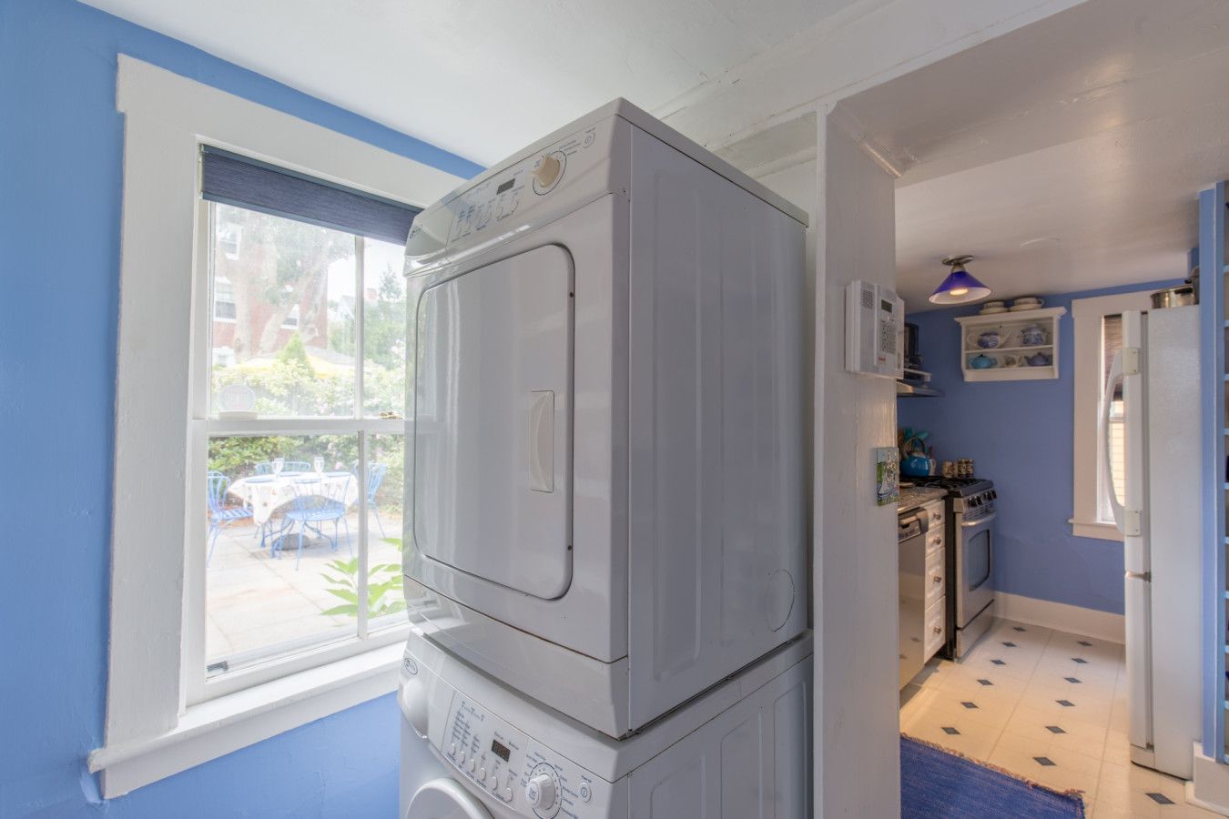 Een kleine wasruimte met een wasmachine en droger, een raam met uitzicht buiten, en een keuken met kastjes en een koelkast.