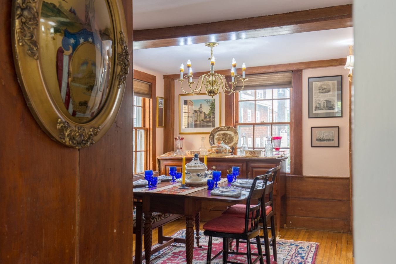 A dining room with a wooden table set for four, a chandelier, and a large mirror.