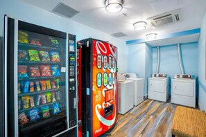A room with a vending machine, a washing machine, and a small kitchenette. - Luxury Oceanfront 1BR | Designer Decor (North Myrtle Beach)