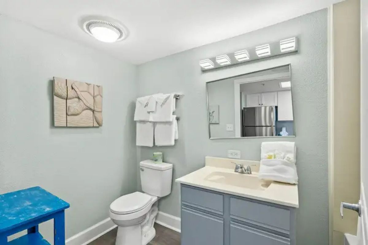 Een badkamer met toilet, wastafel, spiegel en een blauwe kruk.