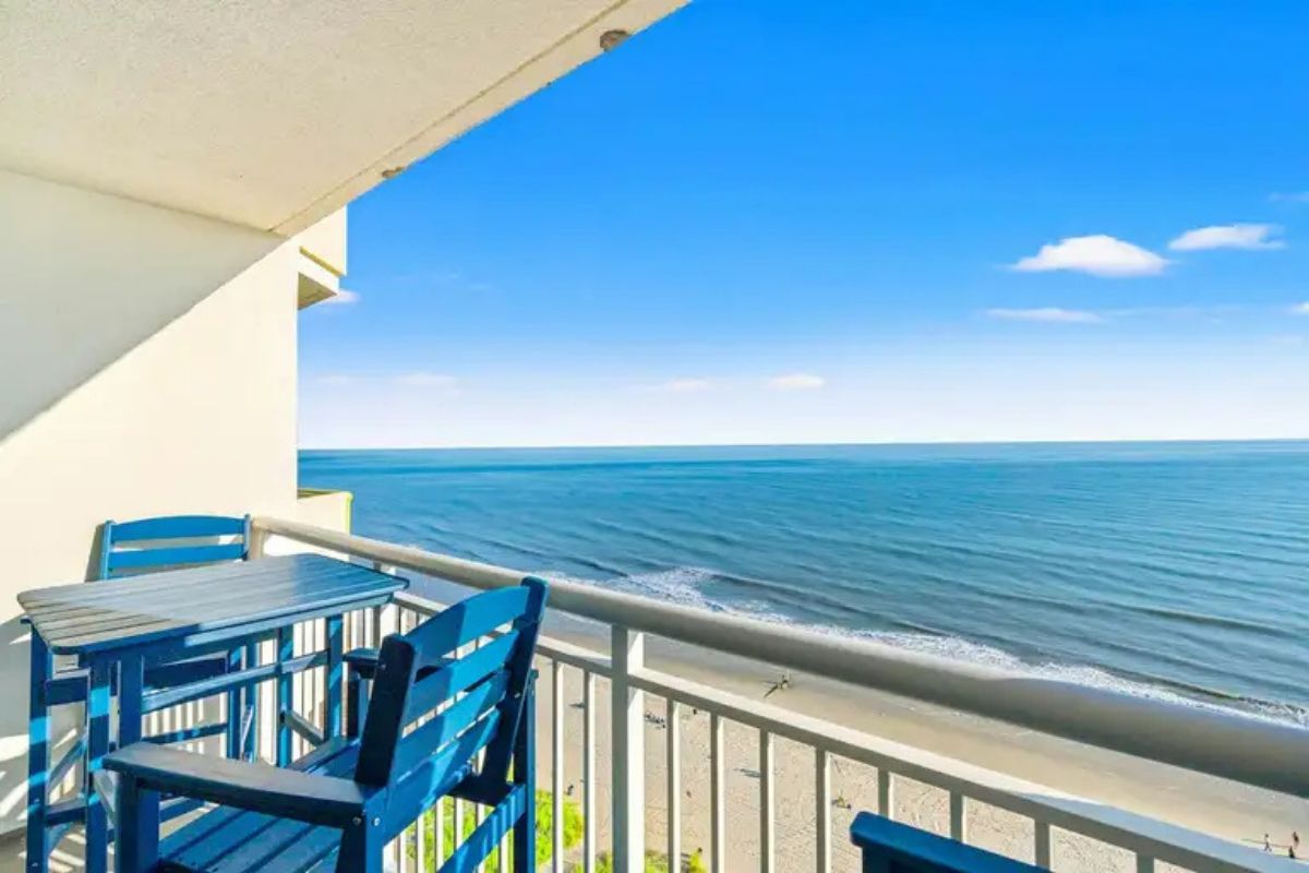 A balcony with a view of the ocean, a table, and two chairs.